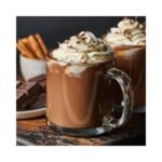 A glass mug filled with Van Houten VH8 Milk Hot Chocolate, expertly prepared by a skilled barista, is adorned with whipped cream and chocolate shavings. In the background at the café, cinnamon sticks and chocolate pieces rest on a small plate next to another partially visible drink.