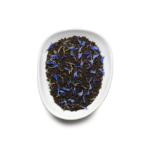 A white bowl filled with loose black tea leaves, accented by vibrant blue and yellow flower petals, reminiscent of the artistry behind Birchall Earl Grey Tea Bags, set against a plain white background.