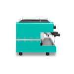 Turquoise espresso machine with a modern, boxy design reminiscent of a barista's tool. It features multiple handles and a stainless steel drip tray, perfect for any café setting. Set against a white background.