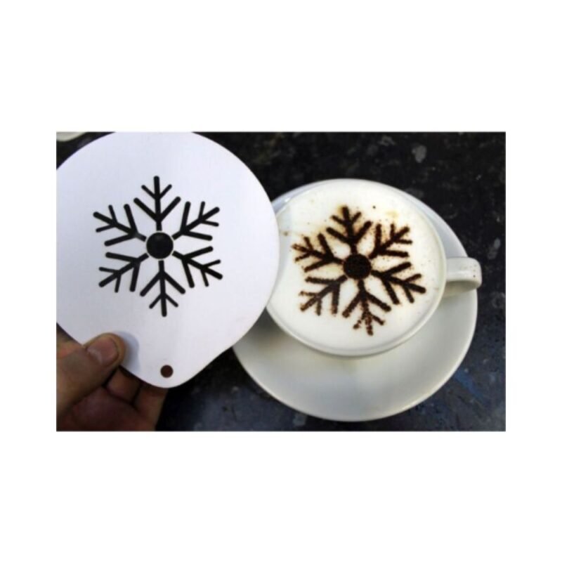 Using the Stencil Snowflake, a skilled barista crafts a cappuccino with a snowflake design on the foam. The café ambiance is enhanced by the cup on a saucer, set against a dark speckled countertop.