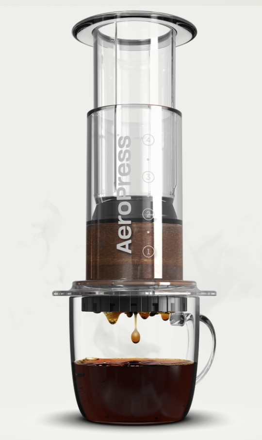 Aeropress portable coffee maker on top of a glass mug producing coffee