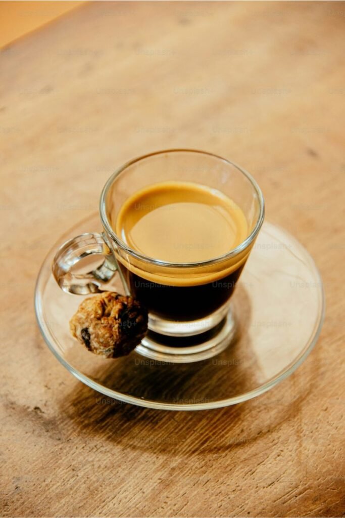 Image shows a cup and saucer with a delicious dark espresso with a good crema, and small biscotti bite to the side.