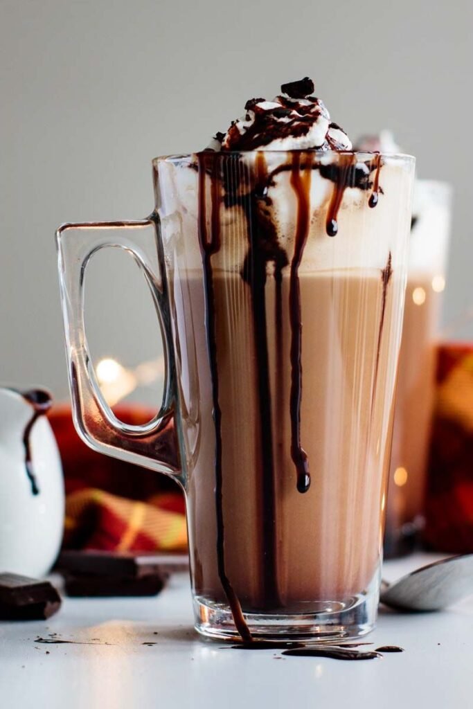 A tall latte style glass of Mocha with fresh cream topping drizzled in chocolate sauce