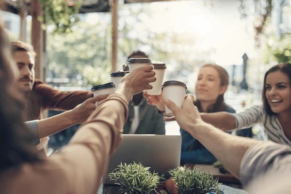 a group of smiling people, raising their cups in cheers to coffee